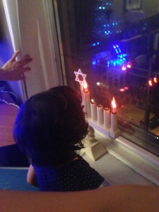 Sienna stares at our menorah (my late grandmother's) as the window reflects our little Christmas tree